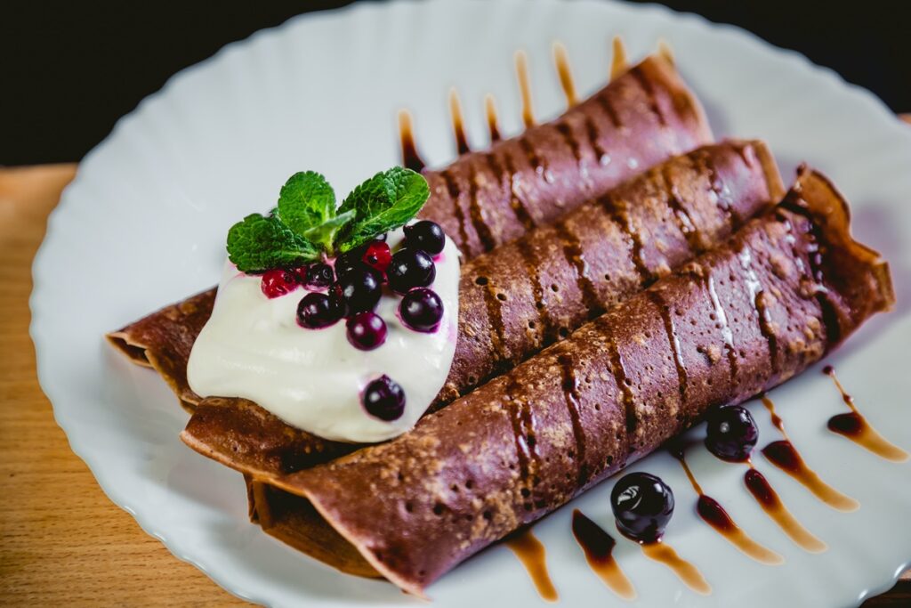 Tiramisu palačinke na krožniku, okrašene s stepeno smetano, meto in sadjem